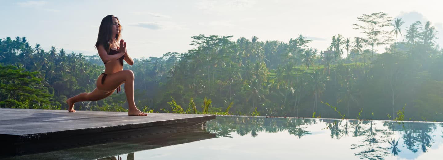 Traveler maintains fitness with a yoga lunge by the hotel pool, surrounded by lush tropical greenery, highlighting wellness options.