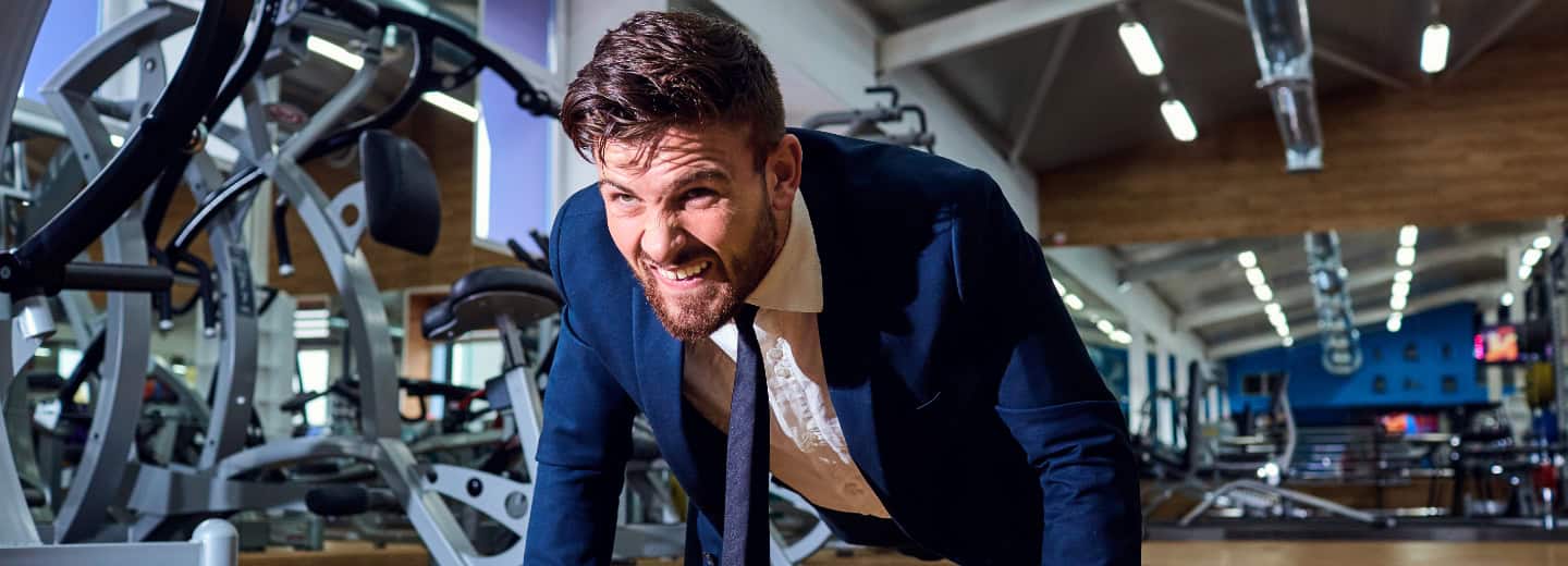 Business traveler in a suit doing push-ups at a gym, staying fit on the go, with gym equipment visible in the background.