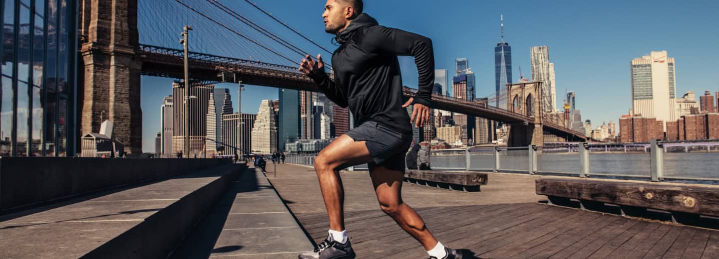 Traveler keeping fit by running on a wooden boardwalk near the Brooklyn Bridge, New York City skyline visible in the background.