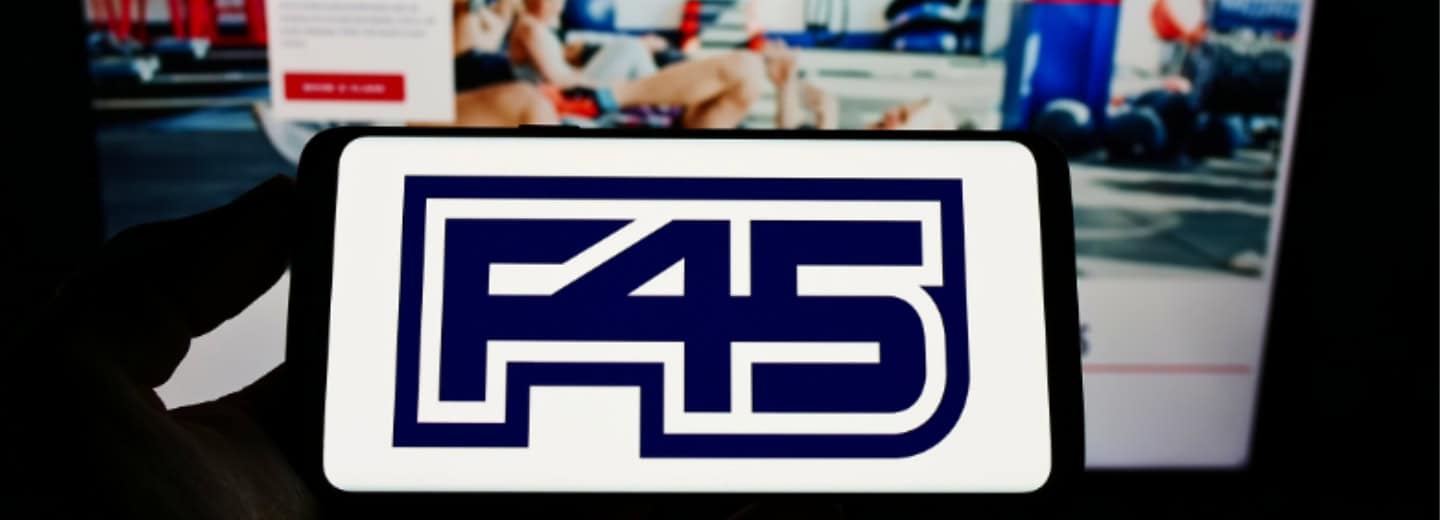 A smartphone shows the F45 logo, with a blurred gym website in the background, highlighting ways to stay fit while traveling.