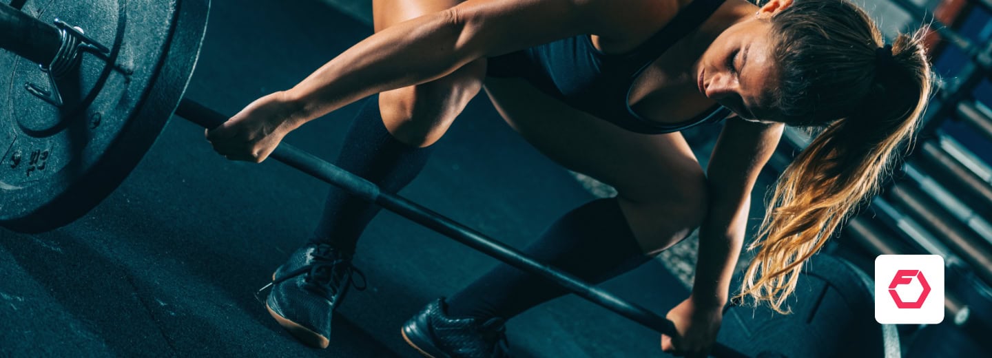 Woman in athletic wear prepares to lift a barbell in a hotel gym, using Fitbod app, showing a way to stay fit while traveling.