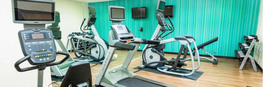 Stay fit while traveling at this gym featuring treadmills, ellipticals, wall TVs, and a dumbbell rack on a wooden floor.