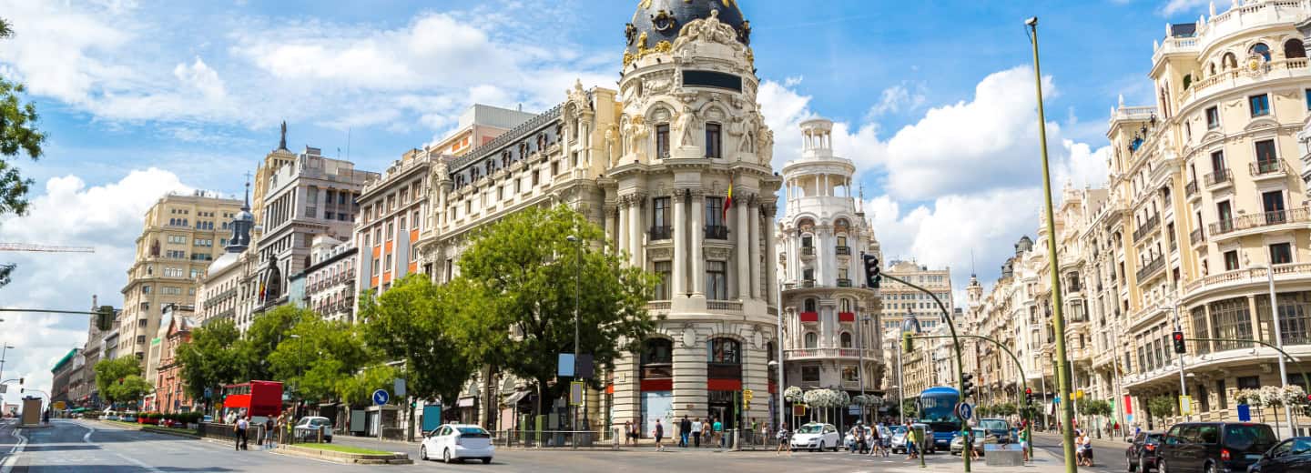 A sunny Madrid street with historic buildings, trees, and active people—perfect for a scenic jog while staying fit on your travels.