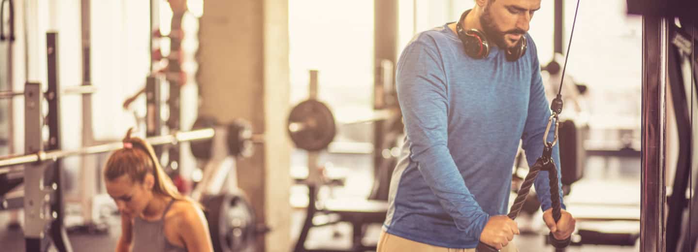 A man works out on a cable machine while a woman sits nearby in a hotel gym, highlighting how guests can stay fit when traveling.