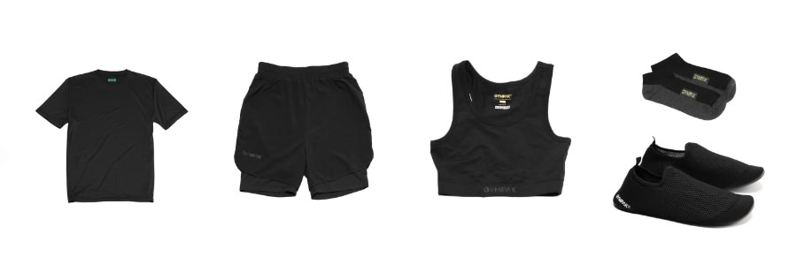 A black t-shirt, shorts, sports bra, socks, and slip-on shoes arranged for a practical travel workout on a white background.
