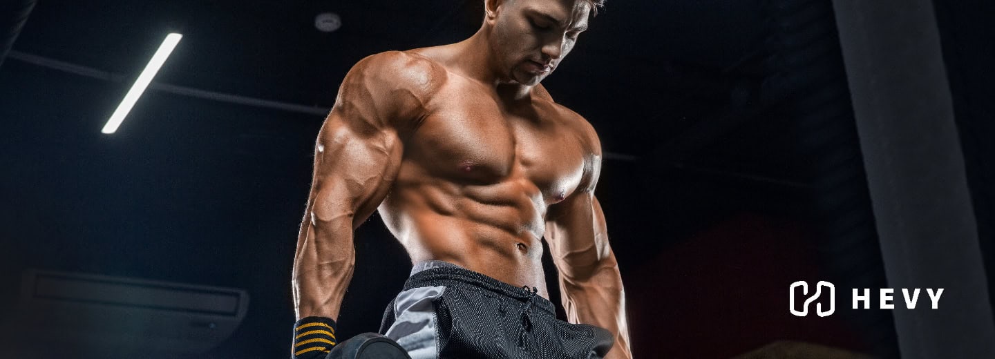 Muscular man in gym shorts lifting a dumbbell, representing staying fit while traveling using Hevy app.