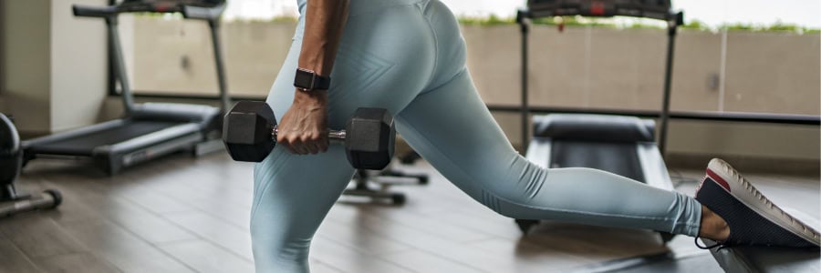 Traveler in workout attire lunging with a dumbbell in a hotel gym, staying active on the road; treadmills behind.