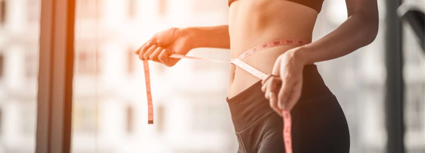 A traveler in workout clothes measures their waist with a tape measure, staying fit on the go and maintaining strength during hotel gym visits.