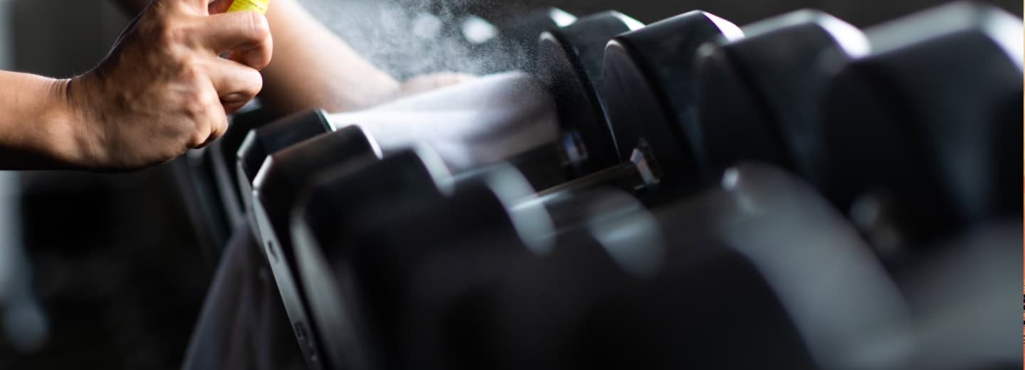 Hand cleaning gym dumbbells with disinfectant. Highlighting safe hotel workouts so travelers can stay fit on the go.