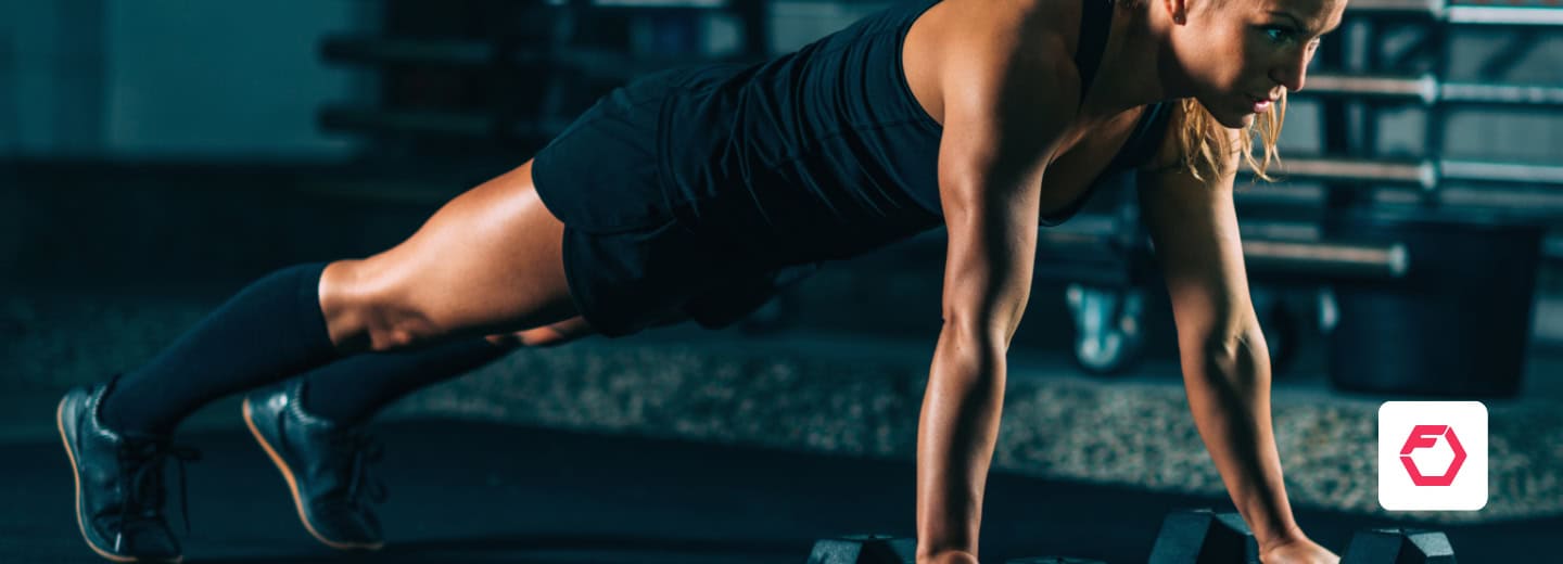 Woman doing a push-up on dumbbells in a hotel gym, using Fitbod app, showing how travelers can stay fit while on the road.