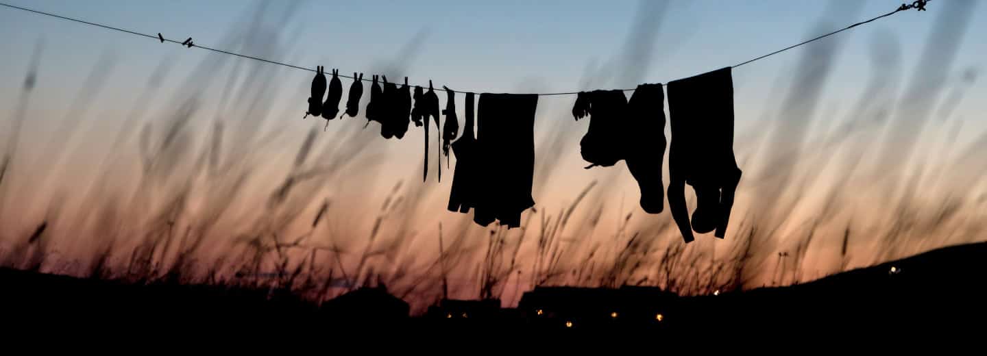 Clothes drying on a line at sunset, suggesting an active traveler’s routine, tall grass and vibrant sky in the background.