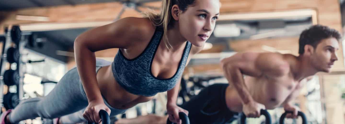 A woman and a man doing push-ups on bars in a hotel gym, staying fit together while traveling.
