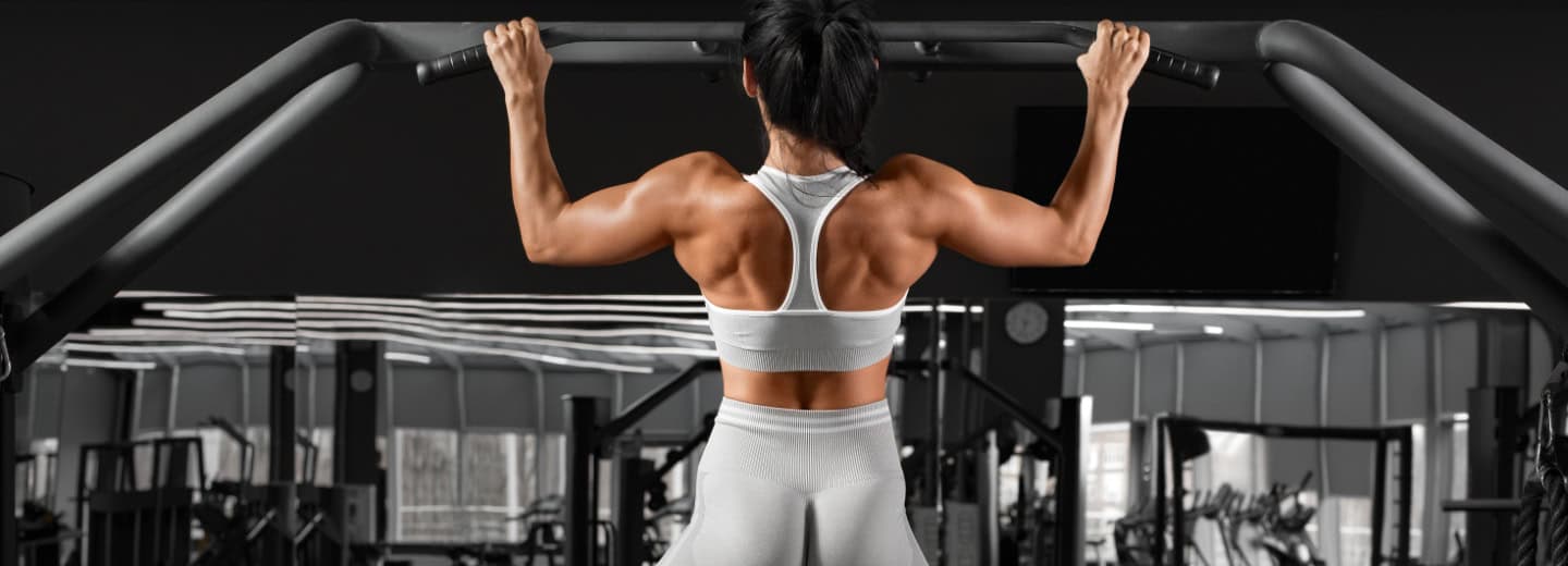 Woman doing a pull-up on a gym machine, showing toned back muscles as she stays fit while traveling.