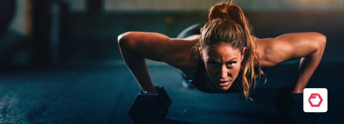 Woman staying fit while traveling by doing push-ups on dumbbells in a hotel gym; using the Fitbod app.
