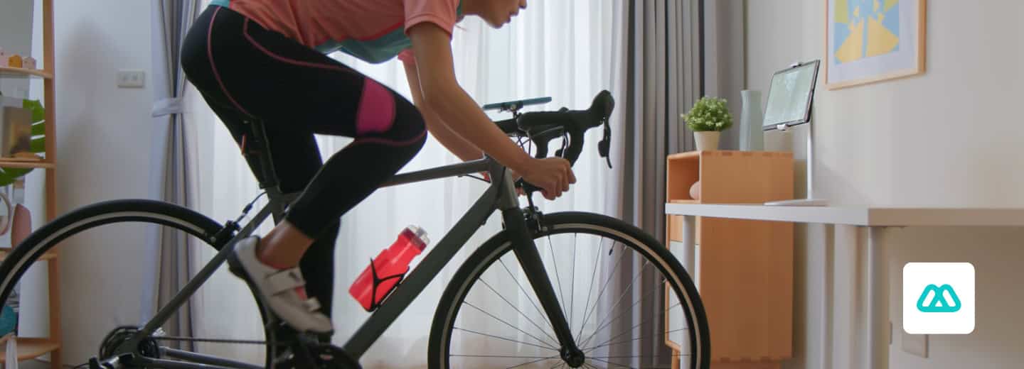 Traveler uses a stationary bike in a bright, using Motosumo app, staying fit with virtual workouts while away from home.