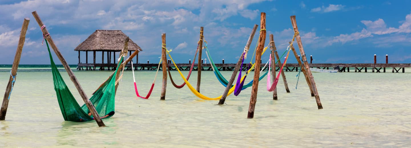 Colorful hammocks hang above beach water by piers in Holbox, offering a relaxing spot to unwind after an active day exploring.