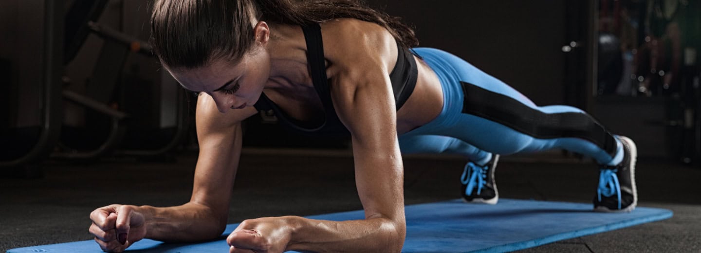 Woman holds a plank in a hotel gym, showing how to stay fit while traveling.