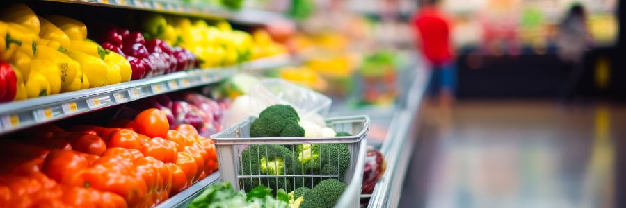 A shopping basket with broccoli and fresh produce sits among colorful veggies, perfect for healthy eating while traveling.