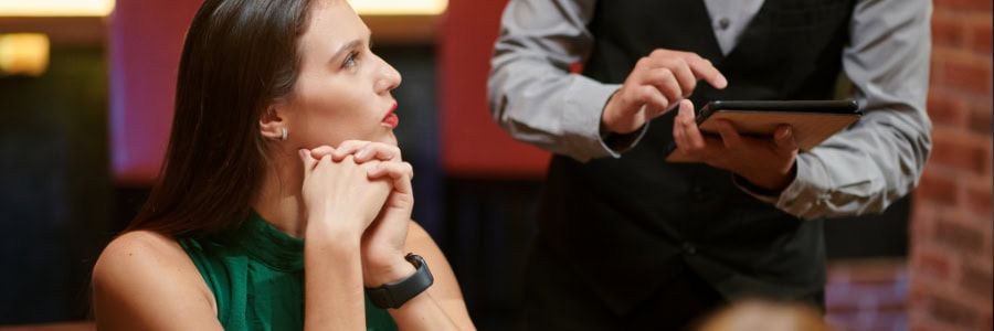 Woman considering a healthy meal as a waiter takes her order on a tablet in a restaurant while traveling to stay fit.