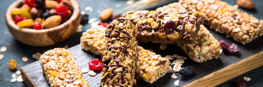 Healthy granola bars with nuts and dried fruits on a slate board, plus a bowl of mixed nuts and berries—perfect for staying fit while traveling.