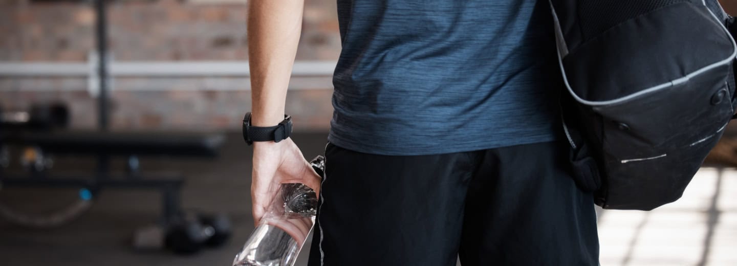 Traveler in gym attire with duffel bag and water bottle stands in a hotel gym, ready to stay fit while on the road.