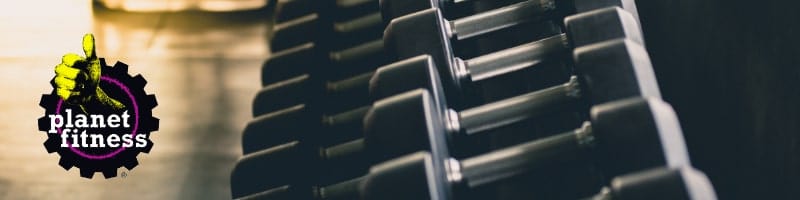 Planet Fitness logo next to a rack of dumbbells, sunlight streaming in, highlighting gym facilities for travelers to stay fit.