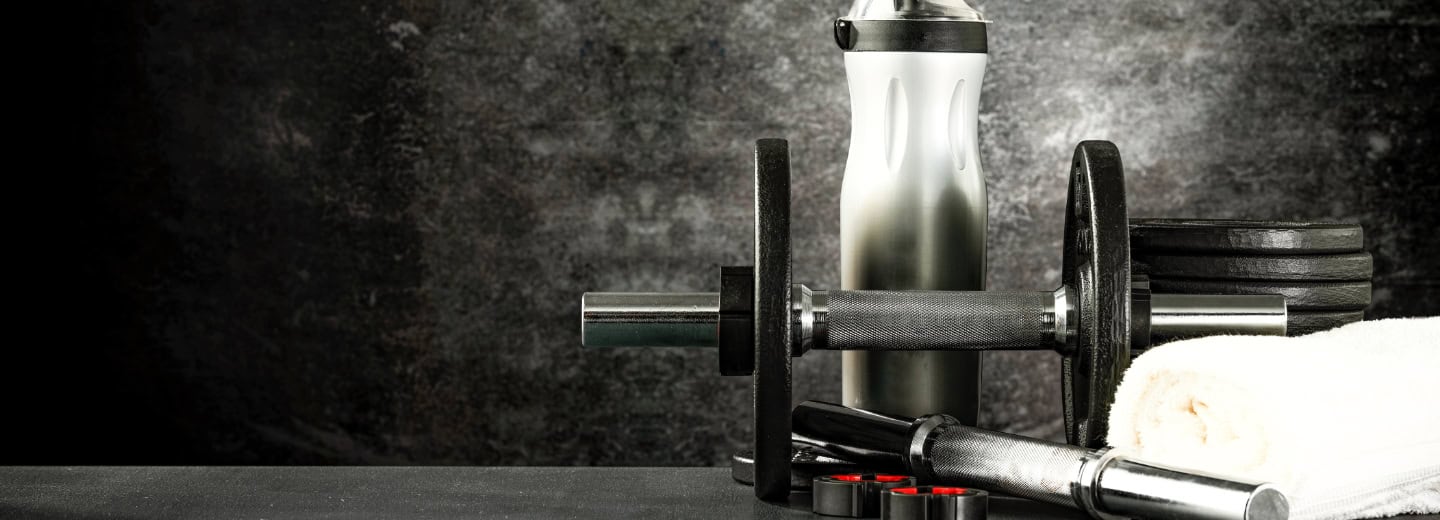 Dumbbell, barbell, weights, towel, and water bottle on a gym bench in a hotel gym—perfect for staying fit while traveling.