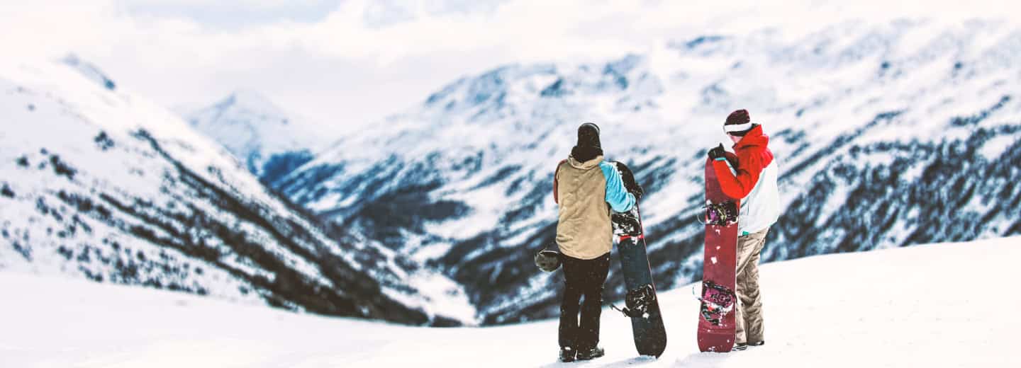 Two snowboarders at a Swiss ski resort overlook snowy peaks, showing how travel can combine mountain adventure and staying fit.