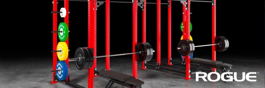Red power racks, weights, and benches in a hotel gym help you stay fit while traveling. Rogue logo appears in the bottom right.