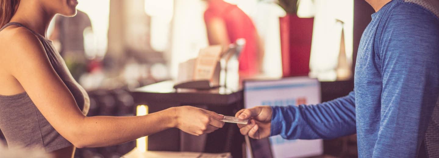 A woman gives a card to staff at a well-lit counter, likely checking into the hotel gym to stay fit while traveling.