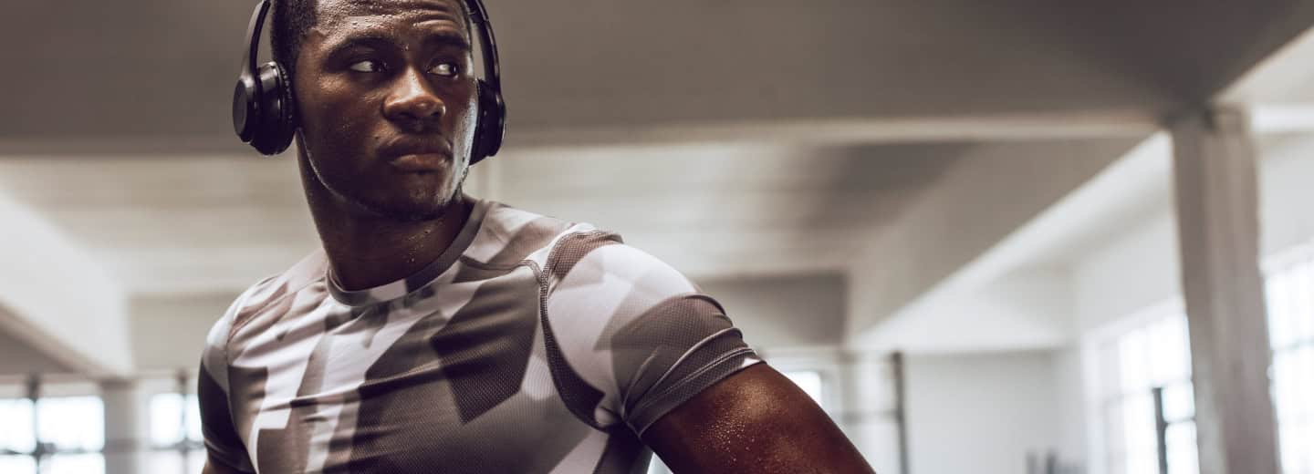 Man in athletic wear with top workout headphones, sweating in a hotel gym, looking aside while keeping fit during his travels.