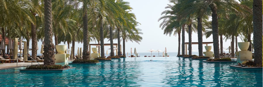 A luxurious pool lined with palm trees overlooks the ocean, offering lounge chairs and umbrellas, perfect for post-workout relaxation.