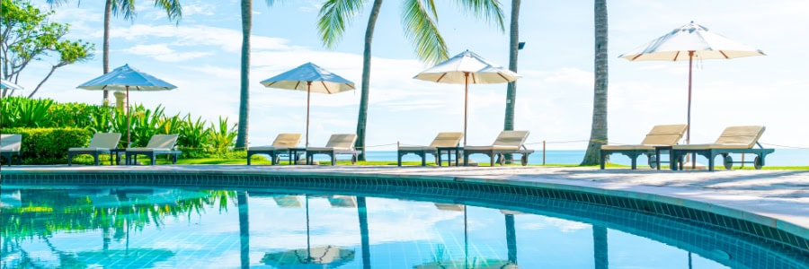 Poolside lounge chairs and umbrellas, palm trees, and ocean views, inviting setting for post-workout relaxation while traveling.