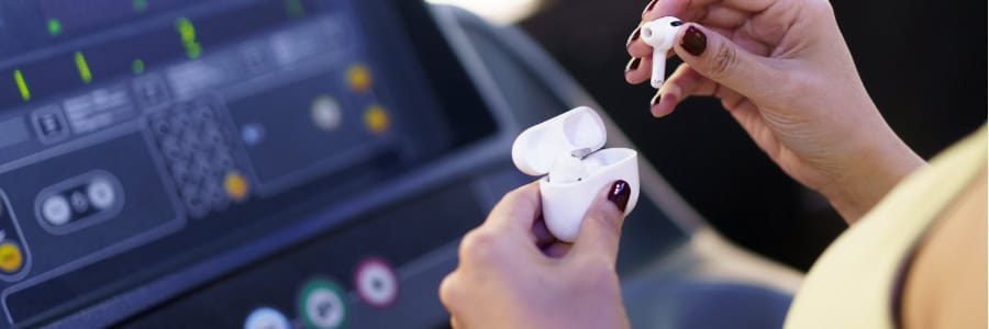 A traveler holds wireless earbuds in front of a treadmill control panel at a hotel gym, staying active while on the road.