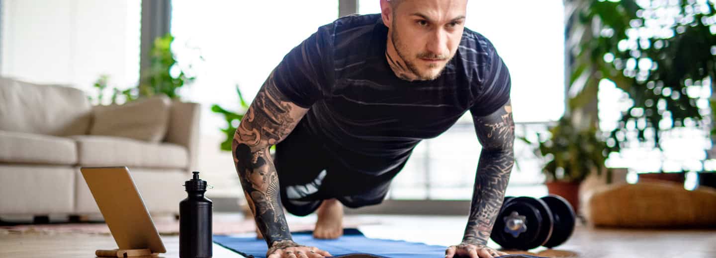 A man doing a push-up on a yoga mat in a hotel room, staying fit while traveling, with water bottle and laptop nearby.