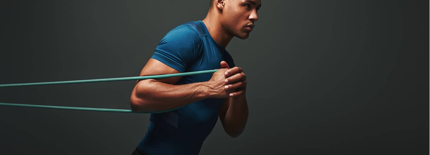 Traveler in a hotel gym stays fit by exercising with a resistance band, leaning forward with determination in a blue shirt.