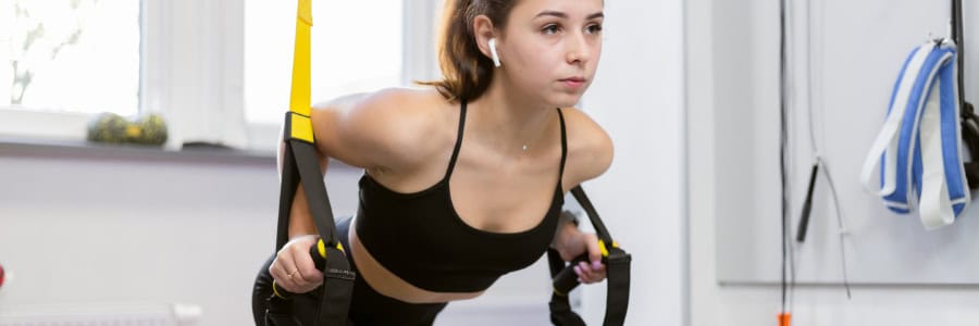 Woman in sportswear uses suspension straps to exercise indoors, showing how travelers can stay fit in a hotel gym.